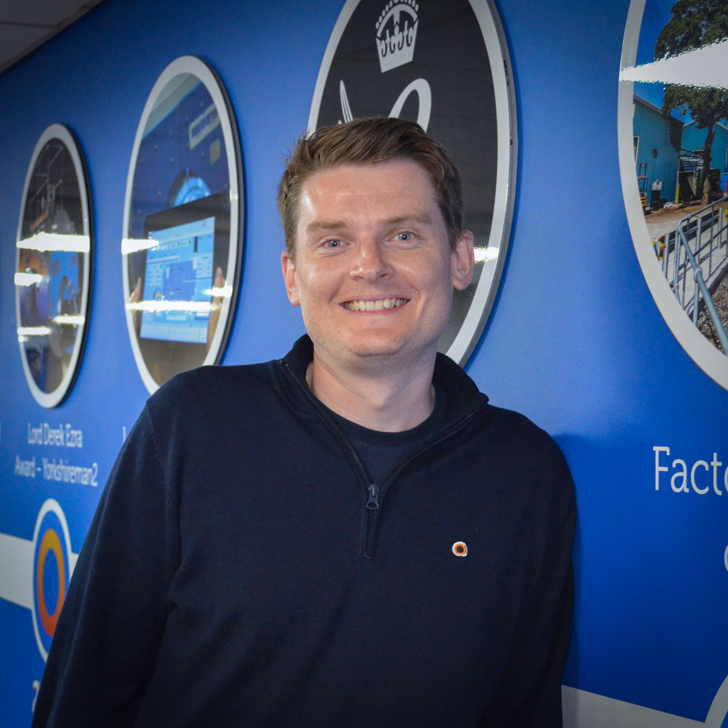 Man in blue jumper leaning on a wall and looking at the camera 